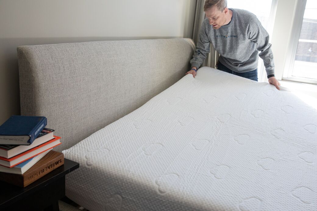 Person placing new mattress on bed