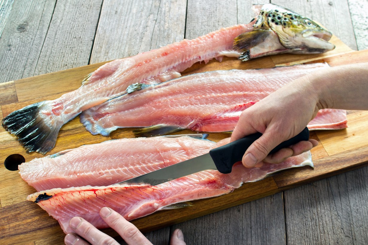 a hand cutting fish meat with a boning knife