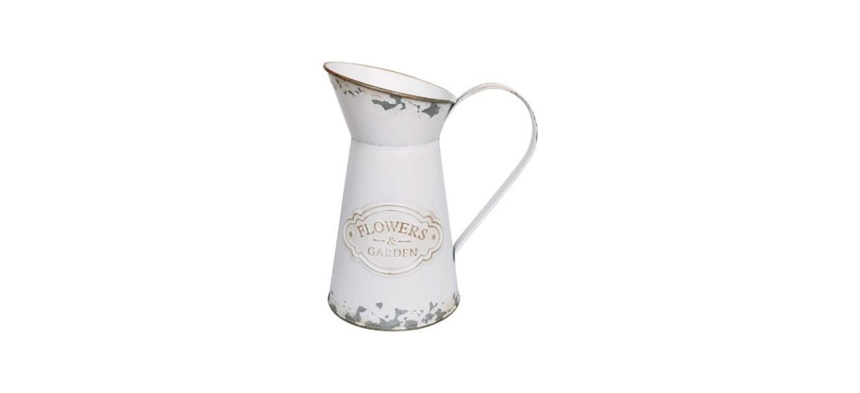 A distressed, metal vase, painted white, shaped like a milk jug with a handle. Text on it reads: Flowers &amp; Garden.