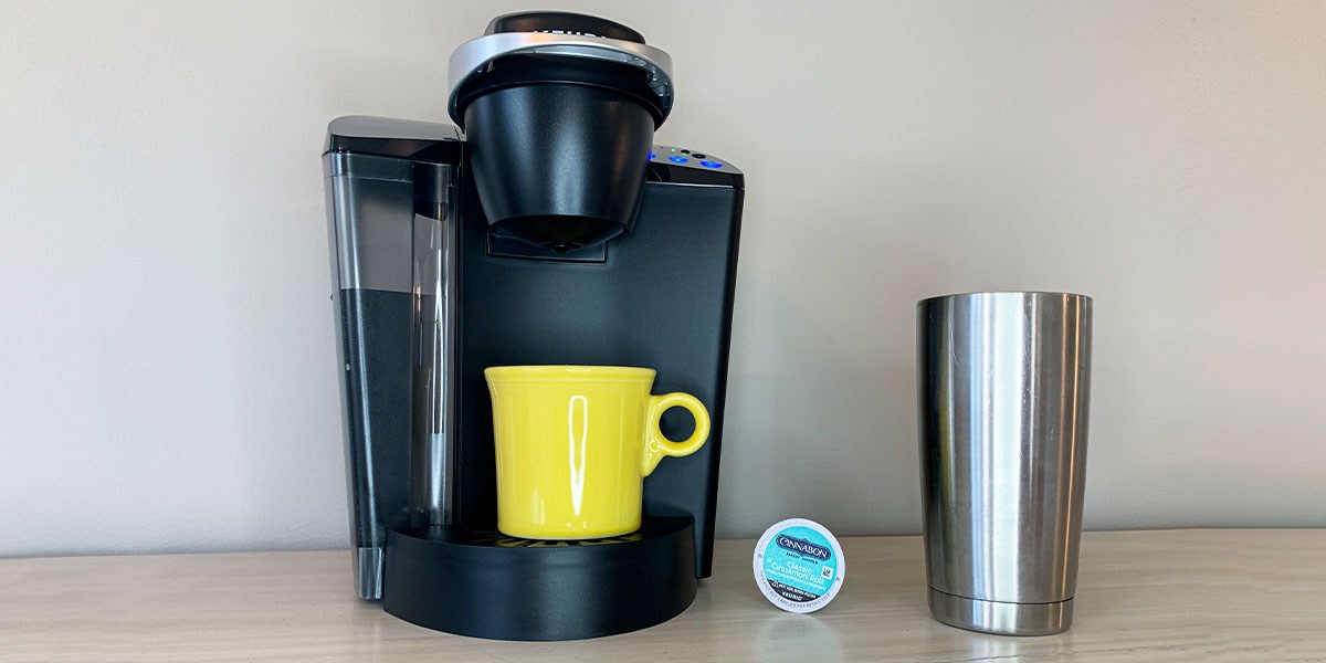 Keurig coffee maker on countertop next to coffee pod and tumbler