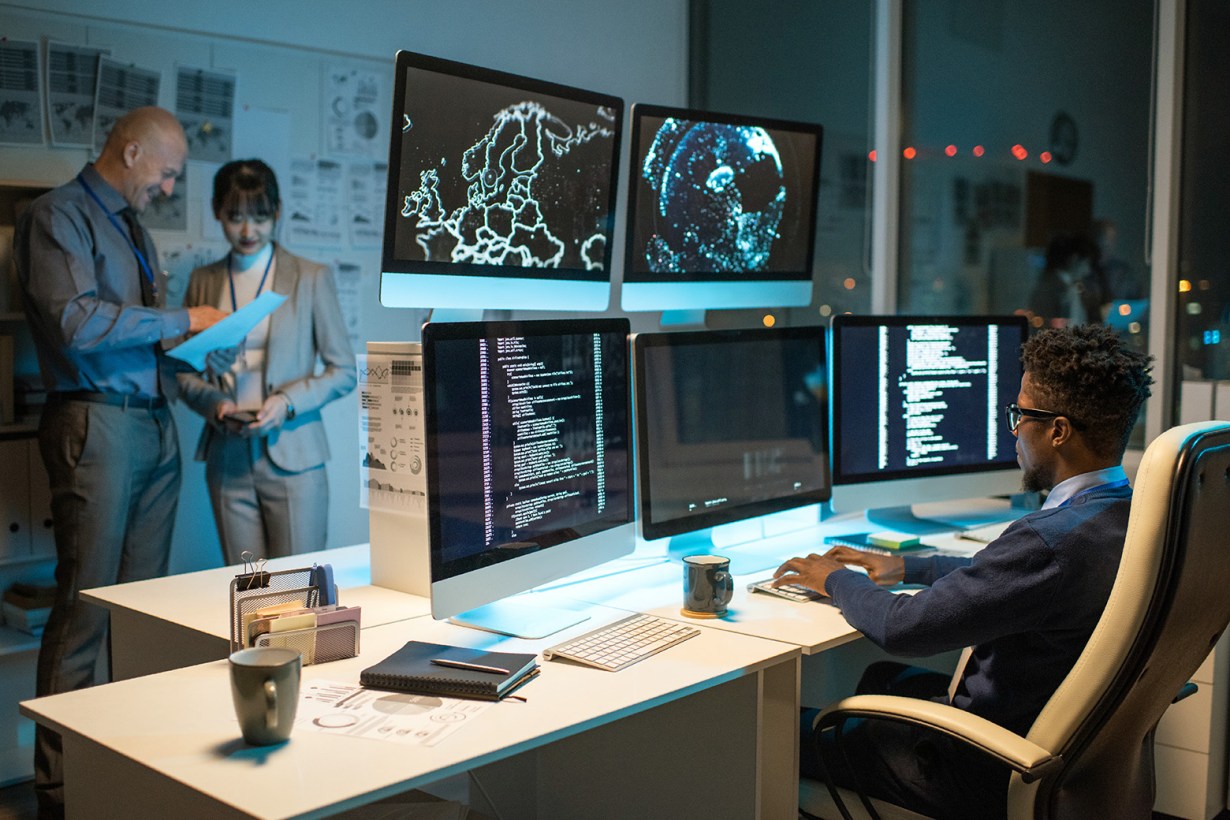 man in glasses in front of five monitors