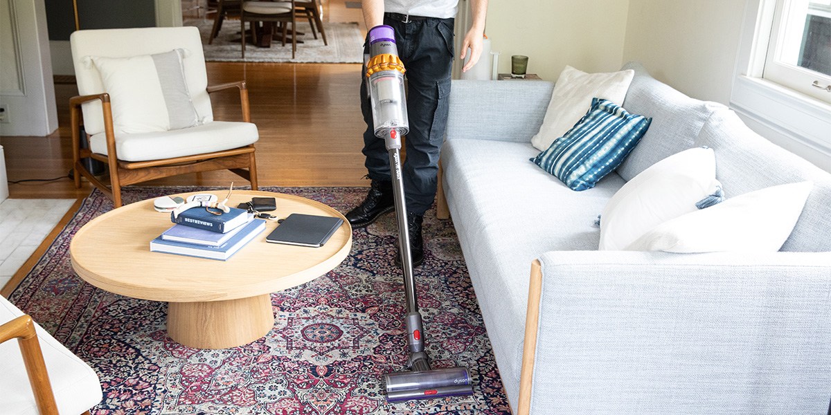 Person vacuuming area rug in front sofa with Dyson V15 Detect Person vacuuming area rug in front sofa with Dyson V15 Detect