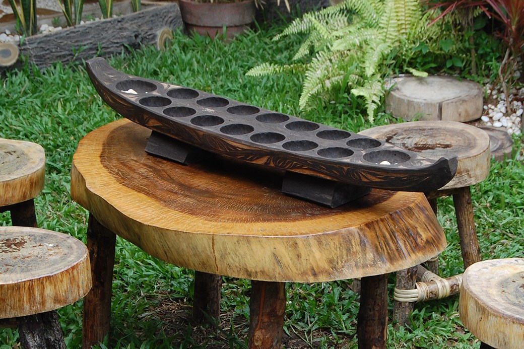 Boat-shaped Mancala board on tree trunk table outside